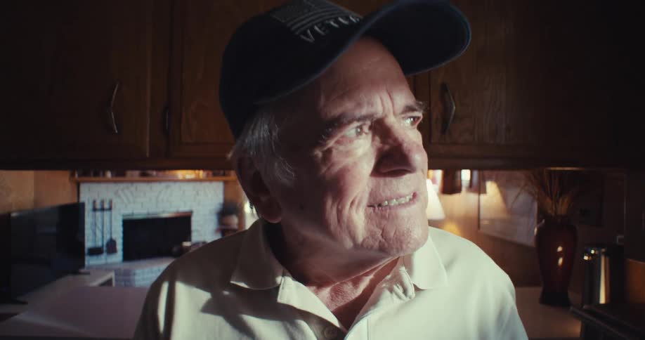 Elderly man wearing a cap with a happy expression while standing in a room of the house
