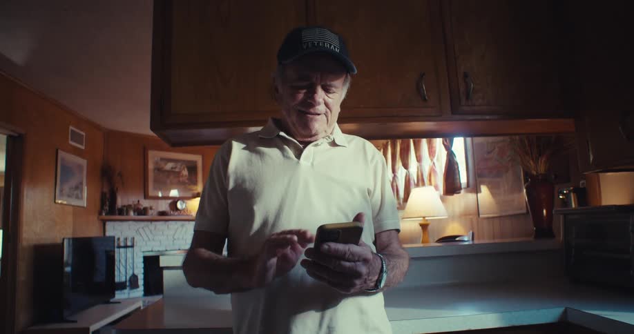 Elderly man in the kitchen laughing while interacting with a smartphone