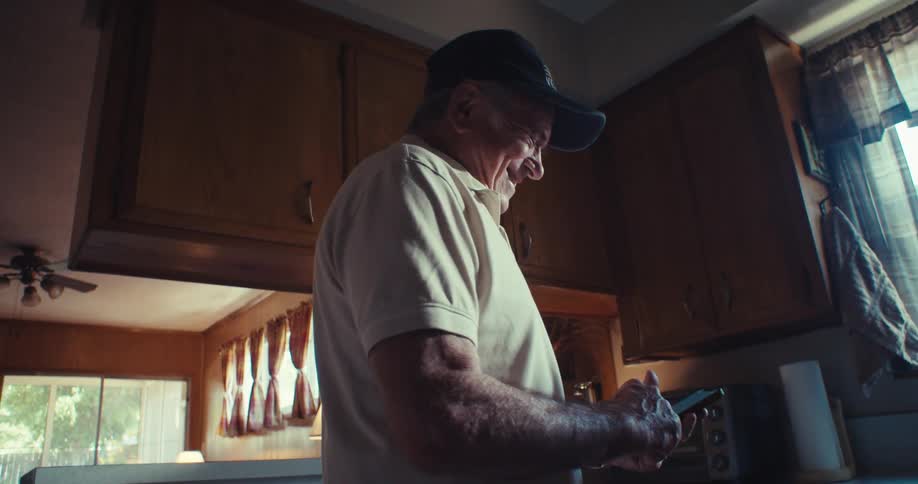 Elderly man with happy expression walking through kitchen and holding a smartphone