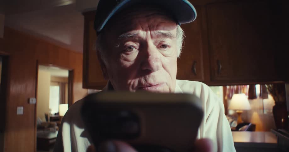 Elderly man wearing a cap talking in front of a smartphone