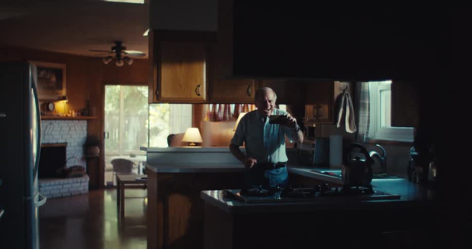 Elderly man in the kitchen watching on his cell phone and celebrating happily