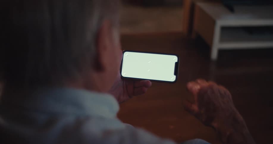 Elderly man waves and smiles while interacting with a smartphone