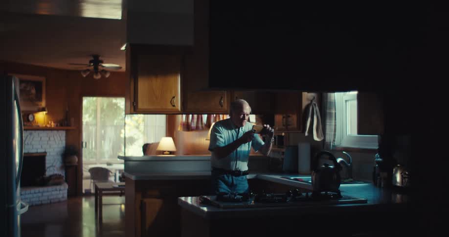 Elderly man in the kitchen holding a smartphone sideways and interacting vibrantly