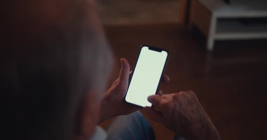 The video features an overtheshoulder shot of an elderly persons hands operating a smartphone with a blank bright screen their fingers are actively tapping and scrolling on the device