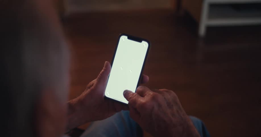 The video features an overtheshoulder shot of an elderly persons hands holding and interacting with a smartphone that has a bright blank screen they are actively scrolling and tapping on the screen