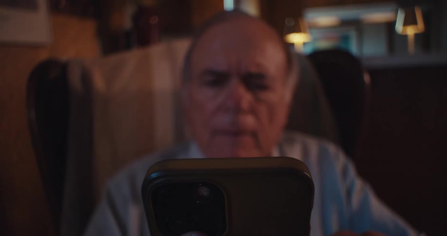 Elderly man sitting in an armchair and interacting with a smartphone