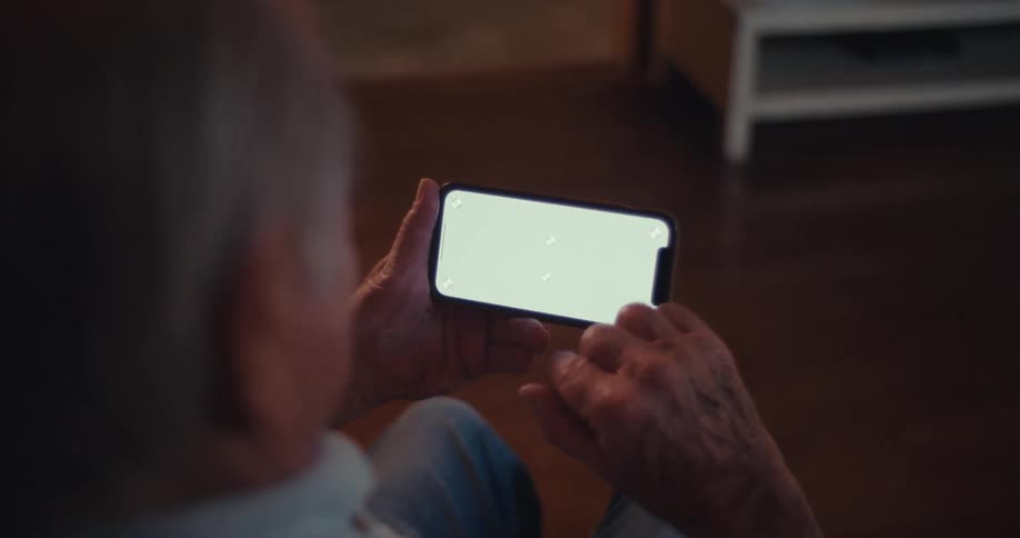 An elderly person sits indoors using a smartphone