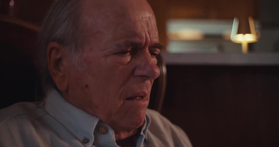 Elderly man sitting in an armchair laughing while holding a smartphone in front of him