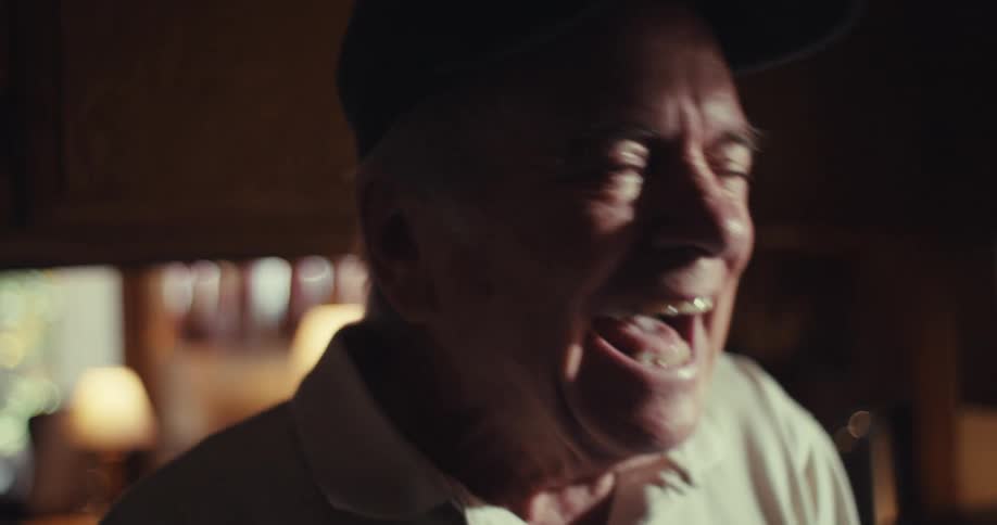 Elderly man wearing a cap laughing while interacting with a smartphone