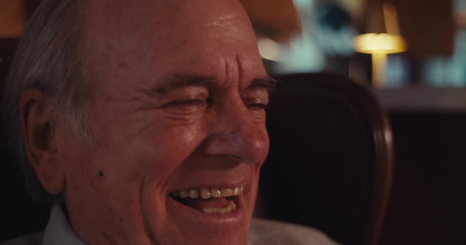 Elderly man sitting in a brown leather armchair laughing and holding a smartphone