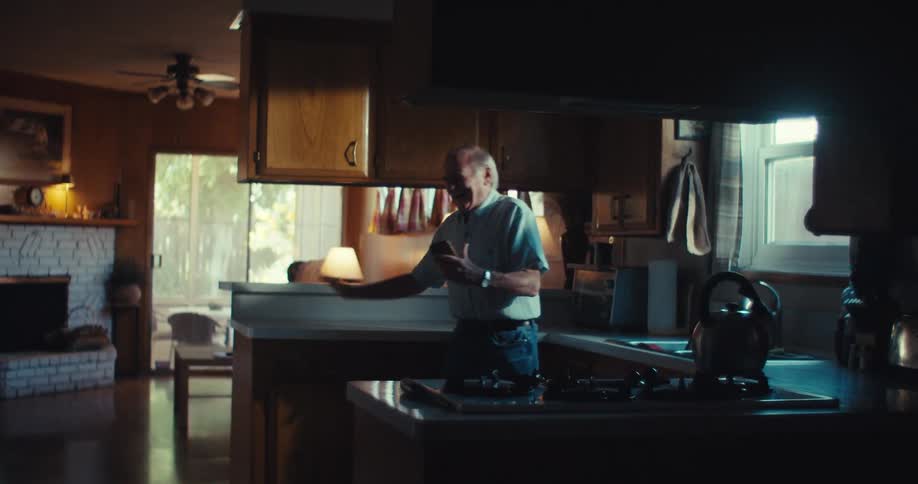Happy elderly man standing in his kitchen facetimeing on his cell phone