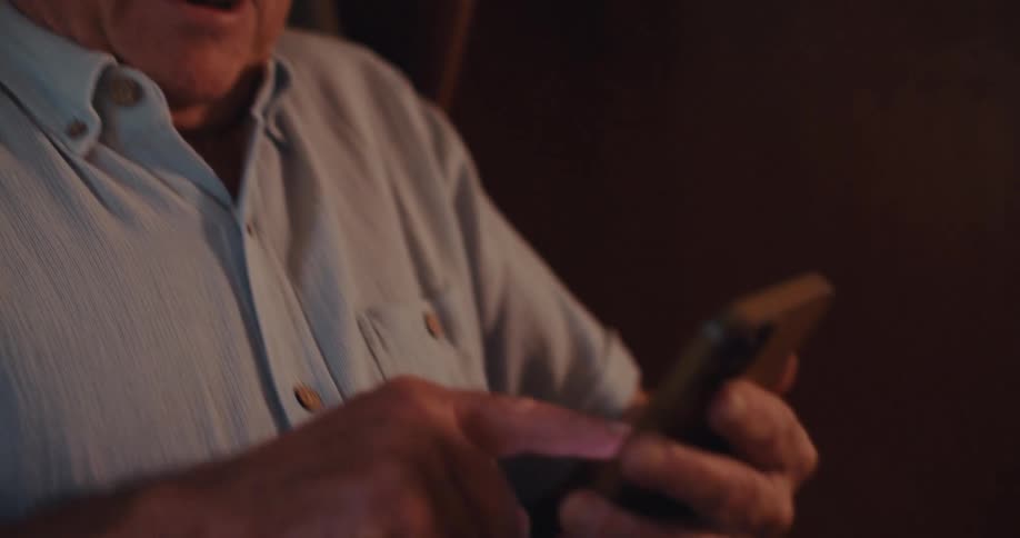 Elderly man sitting with both hands interacting with a smartphone