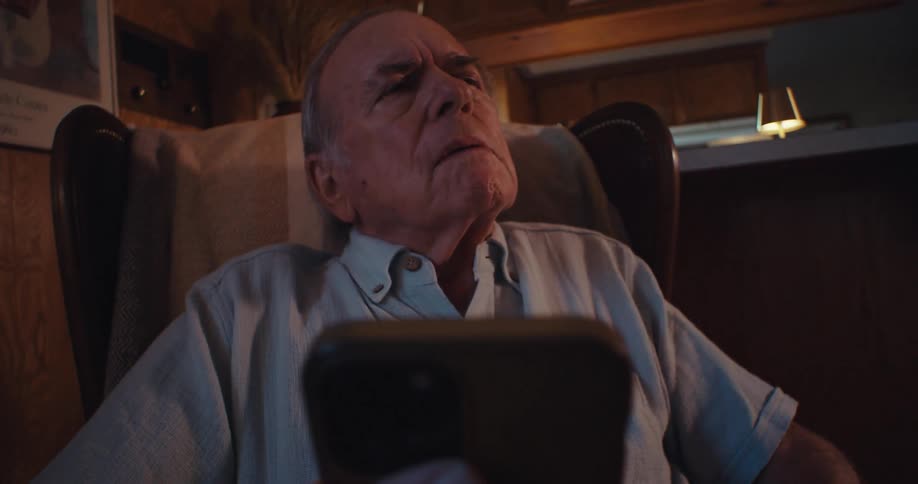 An elderly man looks at his phone with a thoughtful slightly worried expression