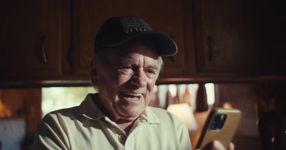 The video features an elderly man wearing a veteran baseball cap looking at his smartphone he appears to be laughing heartily at something he sees on the device