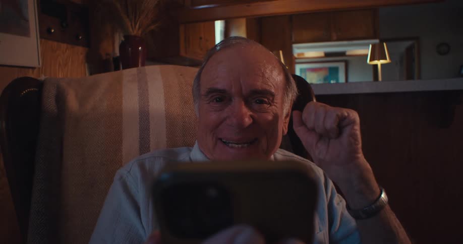 Elderly man sitting and talking in front of a smartphone with a happy expression