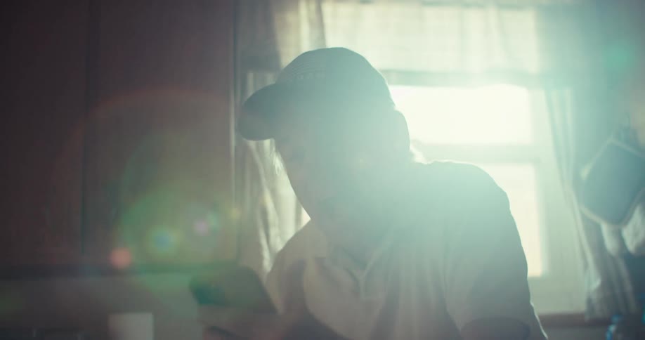 An elderly man laughs joyfully during a video call in a warmly lit kitchen