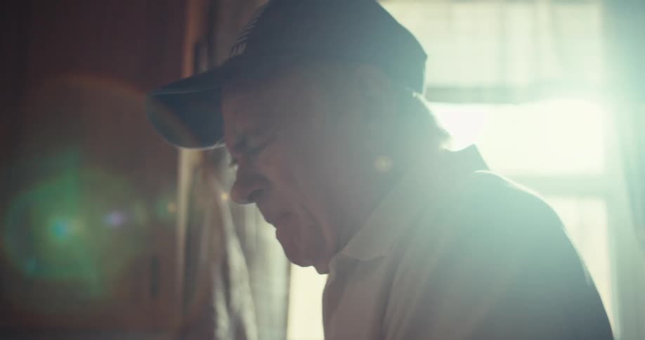 The video features a man wearing a baseball cap with veteran written on it captured in a slightly blurred shot with light flares he is looking downwards and appears to be in thought or reacting to something
