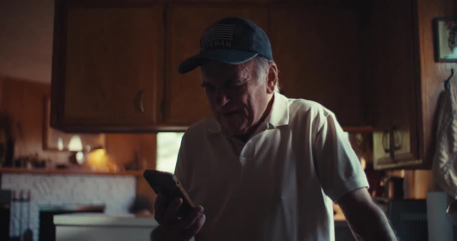 Happy elderly man walking around the kitchen and interacting with a smartphone