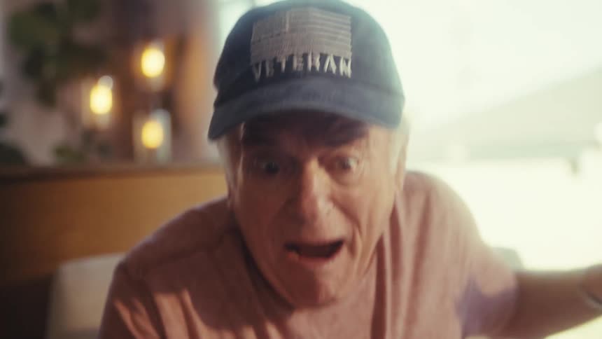 The video features a closeup shot of an elderly man with a concerned expression looking directly at the camera he is wearing a veteran baseball cap and a lightcolored shirt