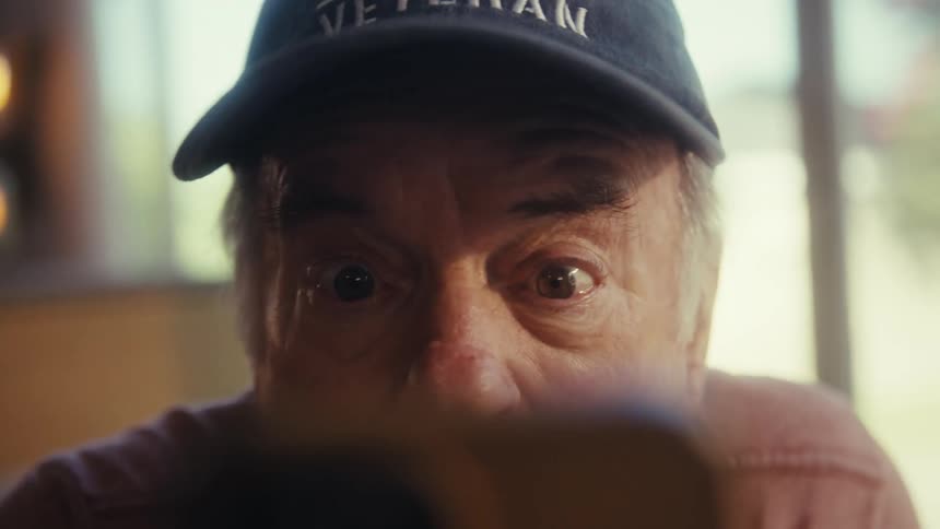 Elderly man widening his eyes in front of a smartphone
