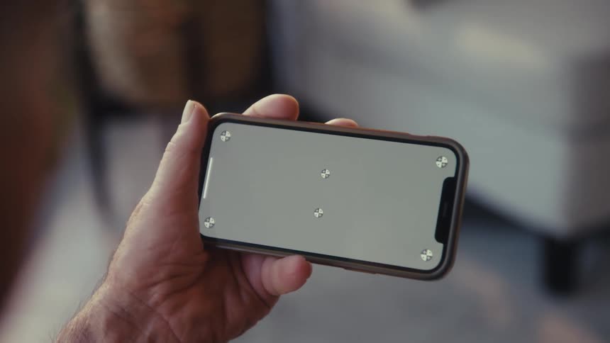 A man sitting in the living room watching a game on his mobile device