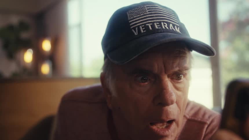 Elderly man looking surprised while holding a smartphone in front of his face
