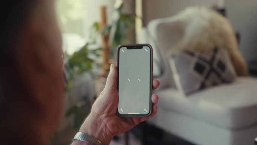 An elderly man holds a smartphone and looks at the screen intently