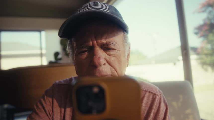 Elderly veteran sitting indoors concentrates on his cellphone screen