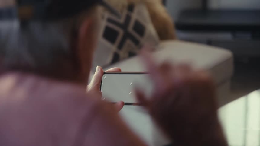 An elderly man holds a smartphone while gaming in a cozy living room