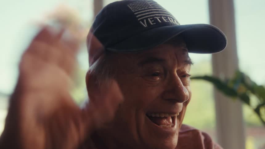Elderly man laughs warmly while waving during a happy video call