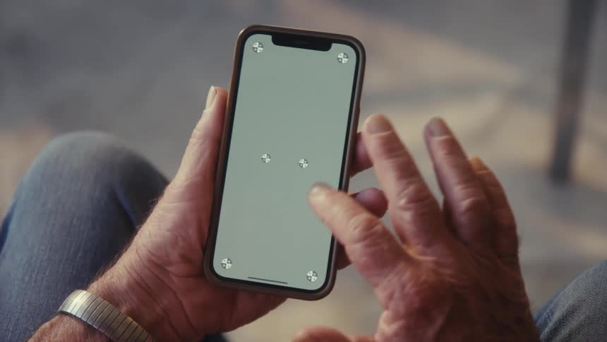 A person with a silver watch on their left wrist holds a cell phone with a blank light gray screen and a gold frame