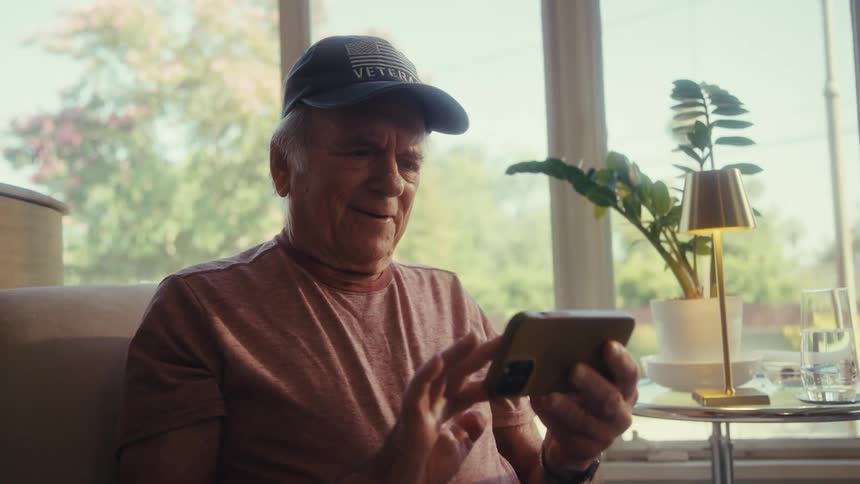 The video features a man wearing a veteran baseball cap sitting in a chair and looking at his smartphone he appears focused on the device