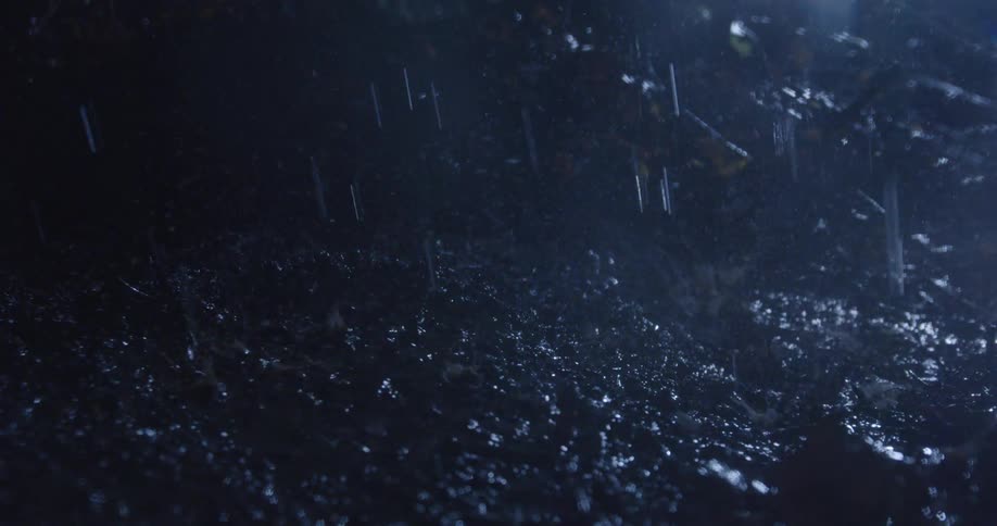 The video shows heavy rain falling creating numerous splashes as drops hit the ground and other surfaces the scene is dark suggesting it might be nighttime or very overcast with reflections visible from the wet surfaces