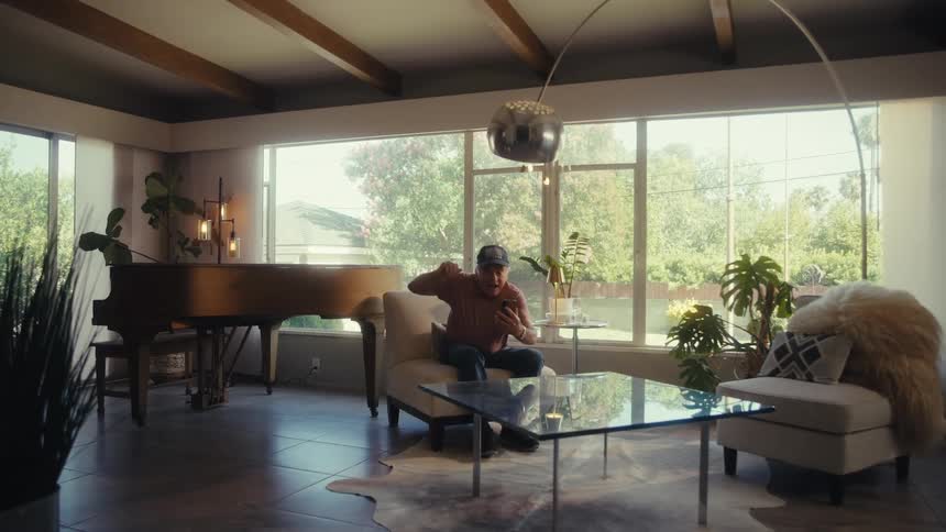 An elderly man is watching a game on his mobile device in his living room with a large glass window at midday he becomes super excited bouncing up and down in his chair