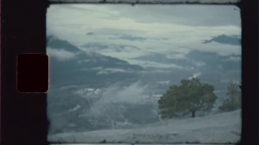 Grainy film frame of misty mountains and a lone tree