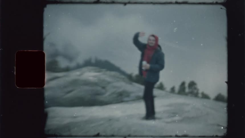 A woman hiking on the mountain wearing a winter jacket waves to a friend