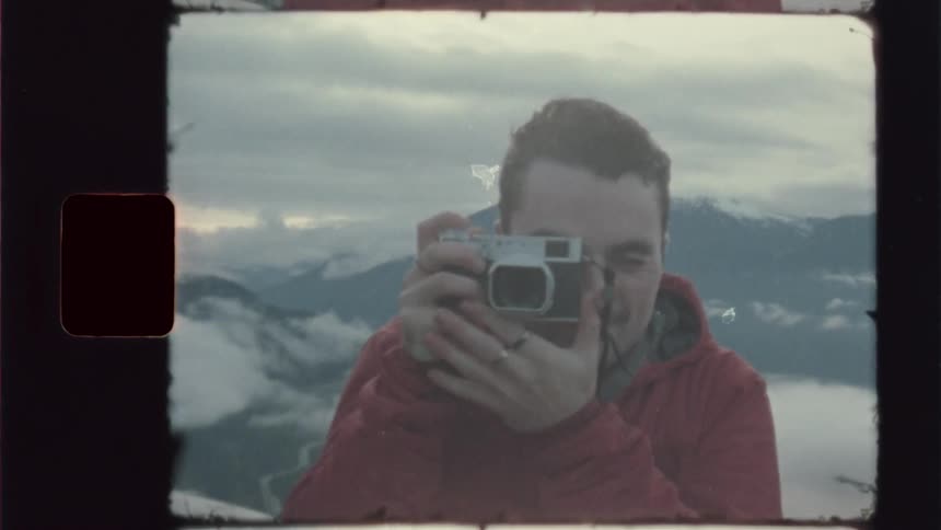 Man on a mountain taking pictures with a vintage camera and a lake in the background