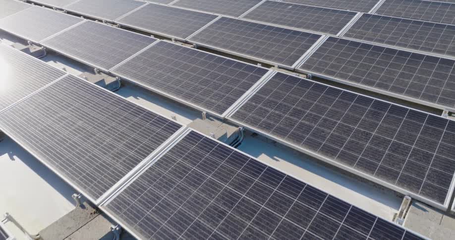 Low and close up skim over an array of rooftop solar panels reflecting late afternoon sunshine