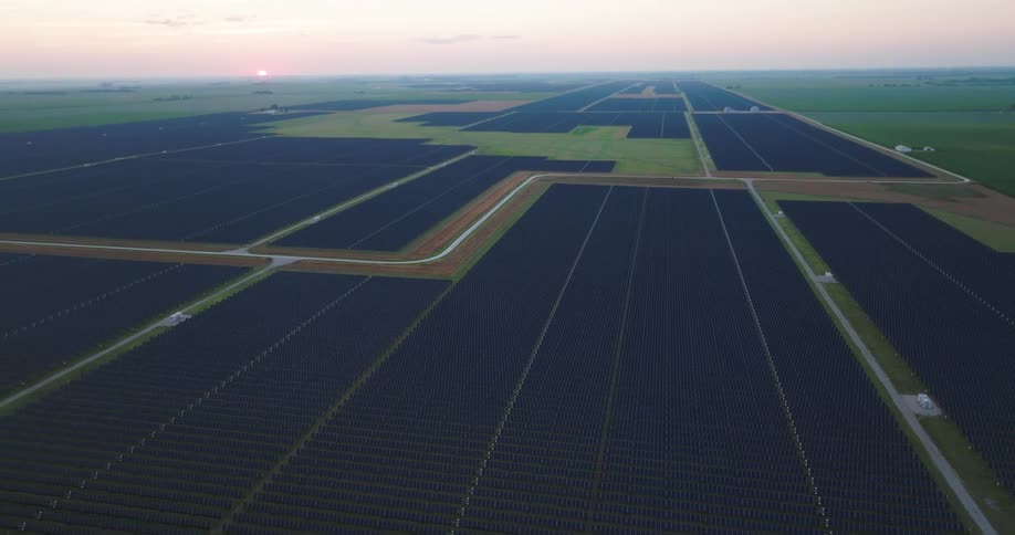 Pullback tilt up reveal of an extremely large solar farm as the morning sun just crests over the horizon
