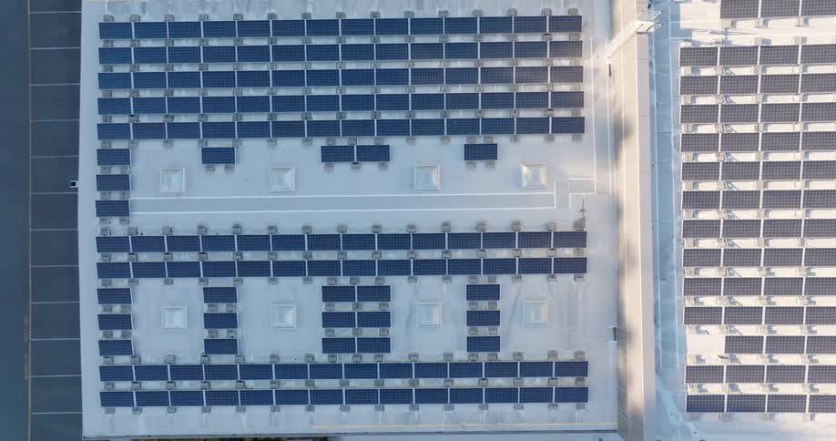 Top down traverse over multilevel rooftops covered in rectangular solar panels neatly arranged in rows