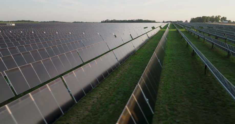 Low skim above long rows of solar panels reflecting soft morning light