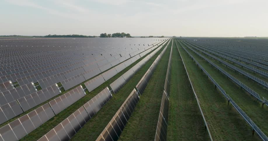 The morning sky is reflected along endless rows of solar panels at a utility scale green power station