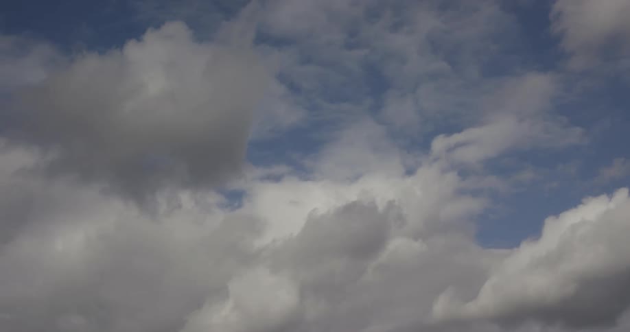 The video shows clouds moving across a blue sky with the sun appearing to be behind them the clouds vary in thickness and shade creating a dynamic sky scene