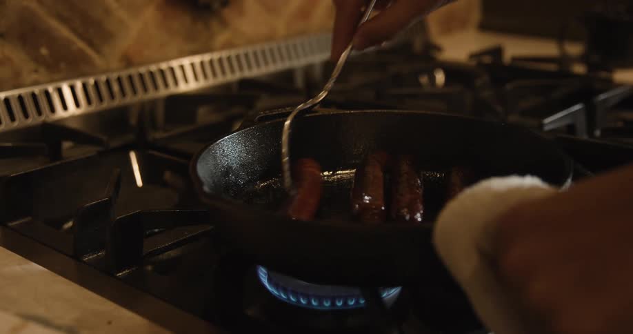 Cooking sausage links in a cast iron pan on a stove