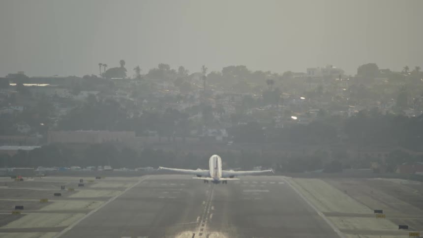 Airplane takes off from runway with hazy city backdrop