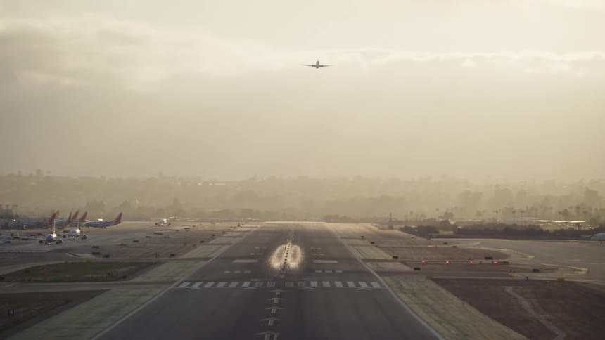 A plane takes off over a runway during a hazy sunrise or sunset