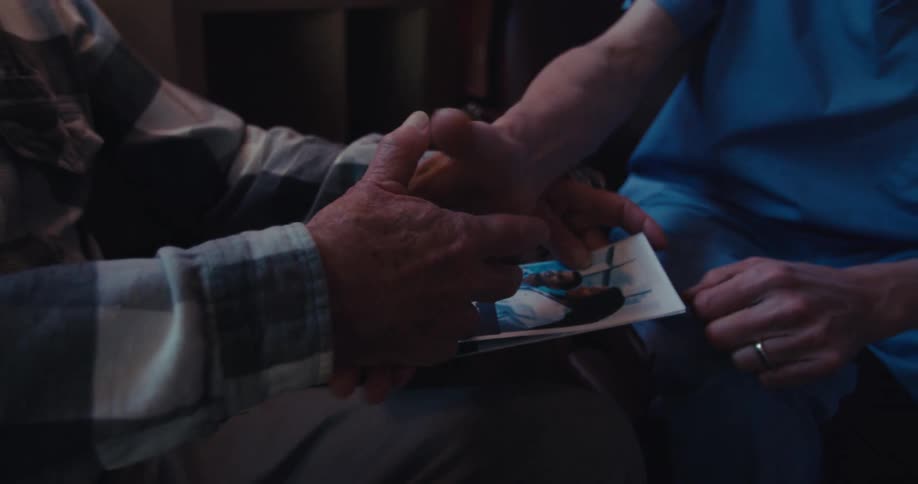 The elderly man holds a healthcare brochure while a caregiver reaches out and they shake hands