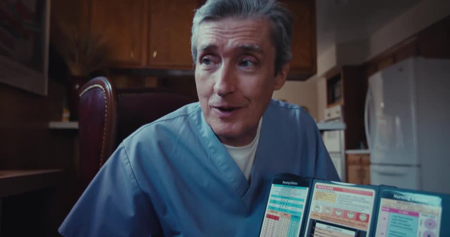 A man in scrubs talks to and points at text in a brochure while chatting with an elderly man