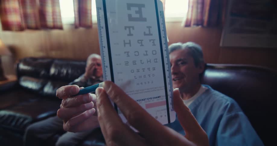 A closeup of an eye chart is shown during an eye exam with both patient and caregiver in the background