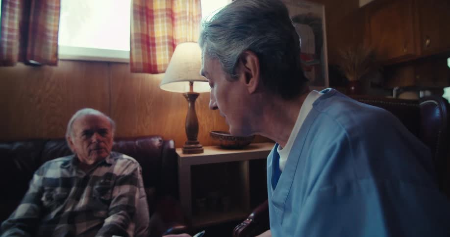 Male medical professional fills out a form while talking to an elderly patient during a home healthcare visit
